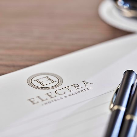 فندق إلكترا متروبوليس أثينا المظهر الخارجي الصورة The photo shows a letterhead or stationery featuring the logo of "Electra Hotels & Resorts." The logo includes a stylized letter "H" enclosed in a circle. There are two black pens positioned on the paper, and a glimpse of a cup, likely with coffee, i