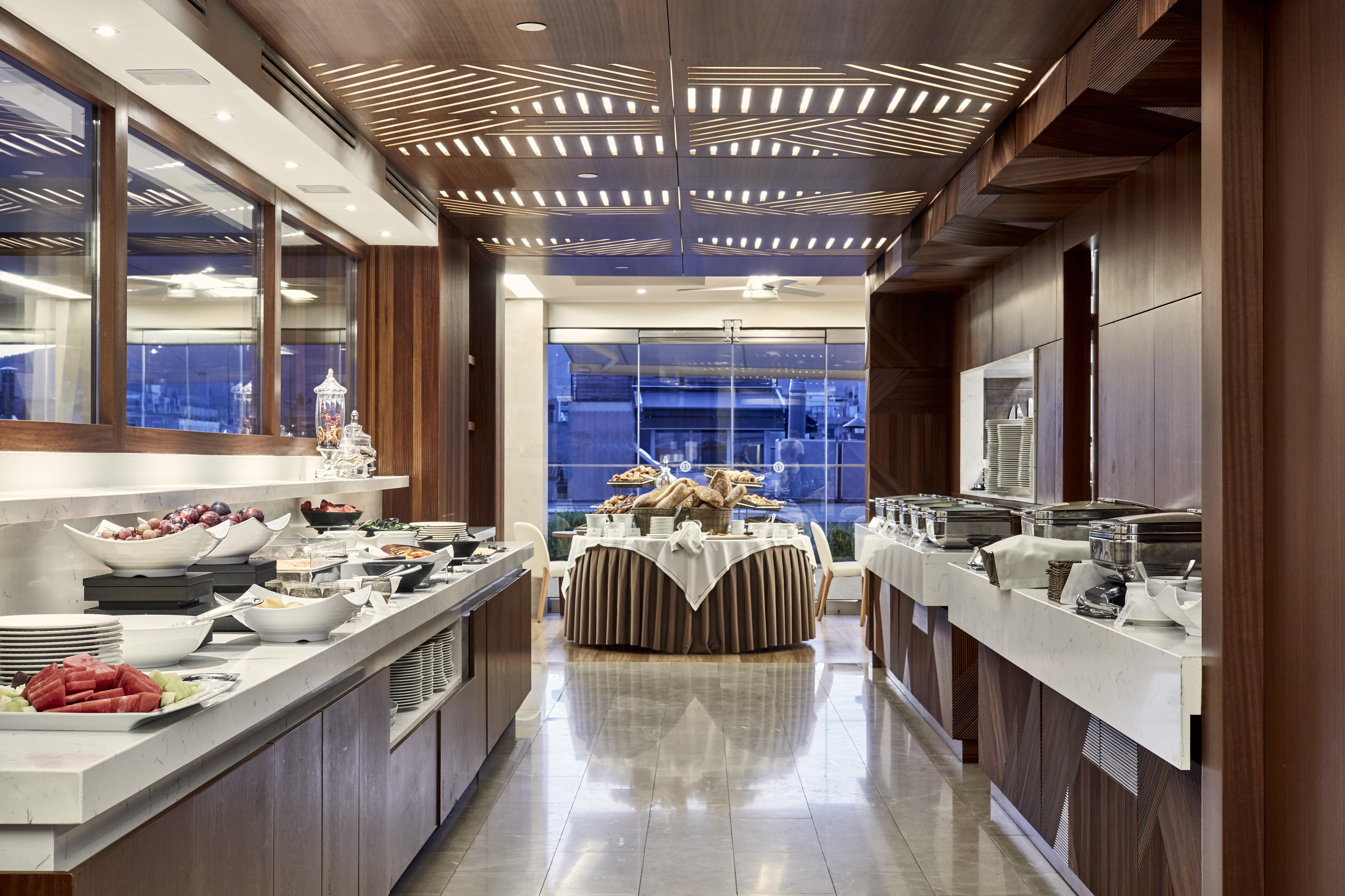 فندق إلكترا متروبوليس أثينا المظهر الخارجي الصورة The photo shows the interior of a modern dining area or buffet setup. The space features elegant wooden paneling and a contemporary design. On one side, there are several buffet tables with an assortment of food items, including fruits and salads, ne